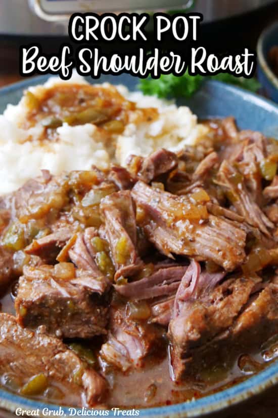 Tender beef shoulder roast shredded and placed on a blue plate with mashed potatoes and gravy.