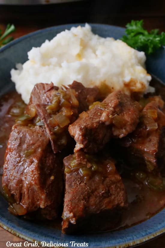 A blue serving dish with mashed potatoes and chunks of beef roast on it.