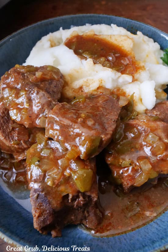 A blue bowl with chunks of slow cooked beef shoulder roast and a serving of mashed potatoes with gravy on top.