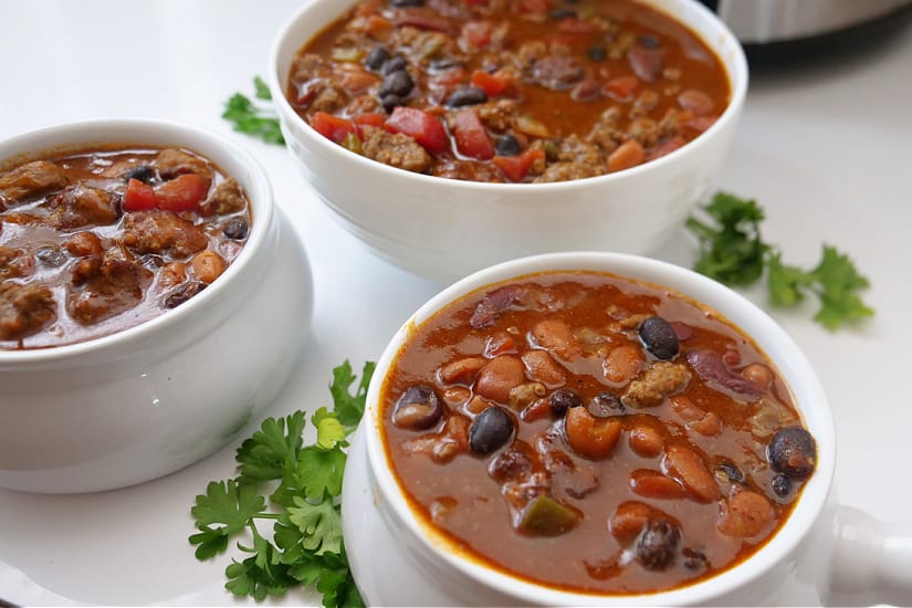 Three white bowls filled with homemade chili all placed on a white surface.