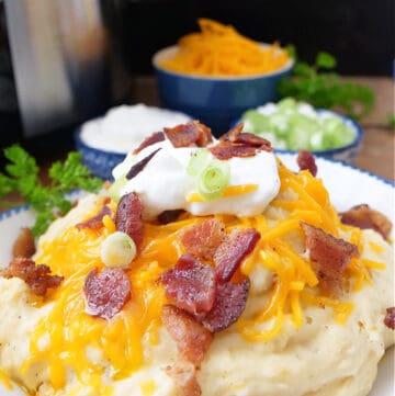 A white bowl with blue trim filled with a serving of loaded mashed potatoes.
