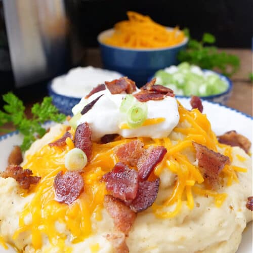 A white bowl with blue trim filled with a serving of loaded mashed potatoes.