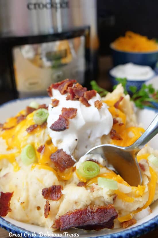 A serving of crock pot potatoes with a spoonful of potatoes being scooped out of the bowl.