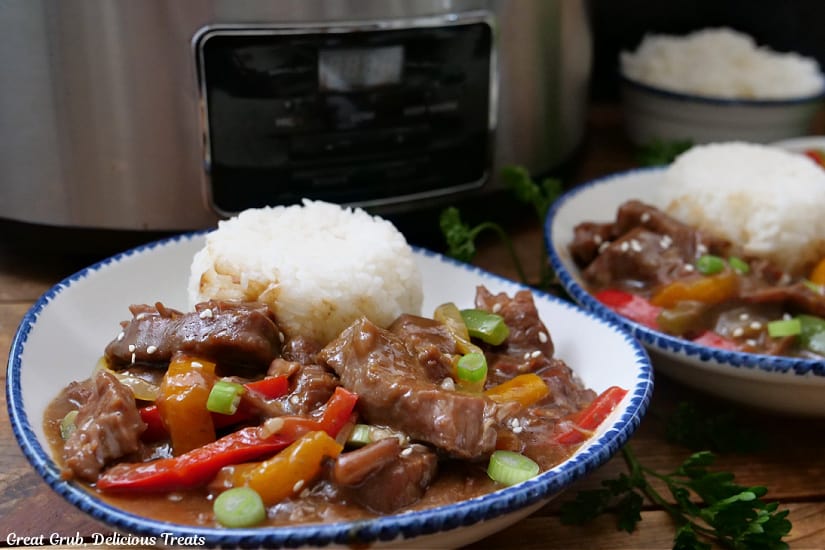 A horizontal photo of two white bowls with blue trim filled with steak and peppers with white rice.