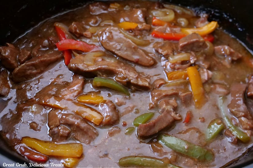 A crock pot filled with steak and peppers.