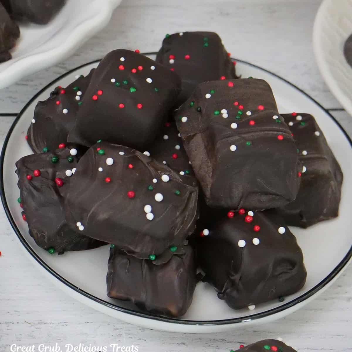 A white plate with a small stack of dark chocolate covered caramel on it.