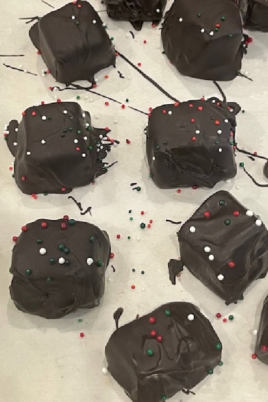 A baking sheet with parchment paper on it with chocolate covered caramel and festive candy sprinkles on top.