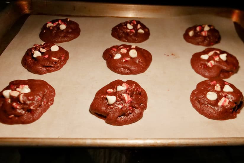 A parchment paper lined baking sheet with nine cookies being baked in the oven.