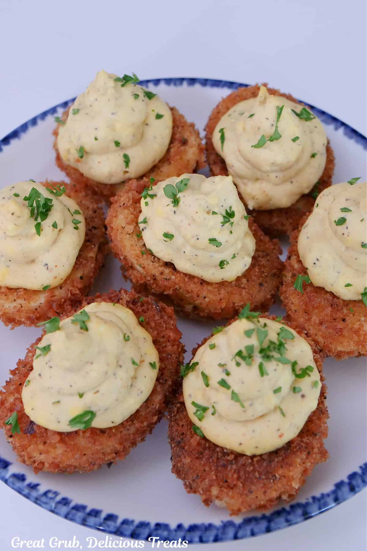 A round white plate with blue trim with seven crispy fried deviled eggs on it.
