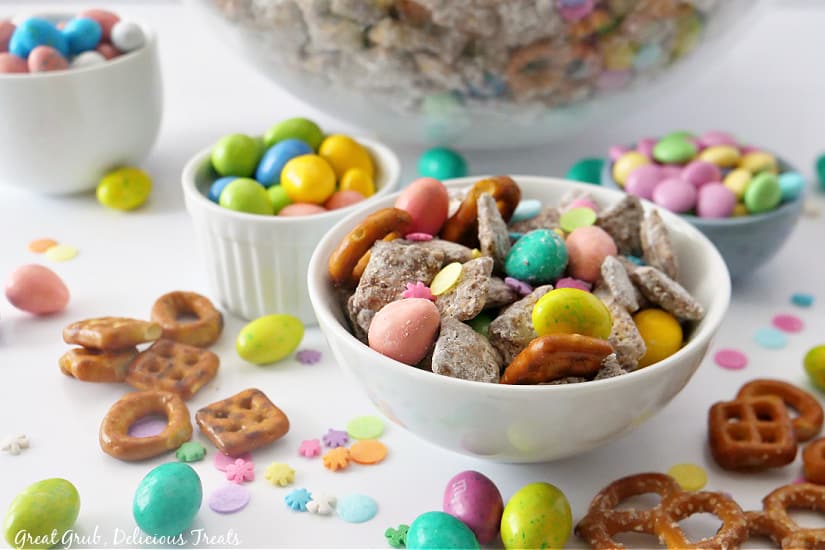 Bowls filled with chocolate candies and one filled with bunny chow and pretzels and more candies laying around the bowls.