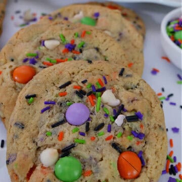 Three big Halloween cookies on a white surface with candy sprinkles scattered about.