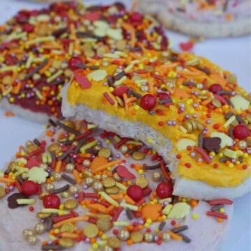 A white surface with big frosted fall cookies on it with a bite out of one of them.