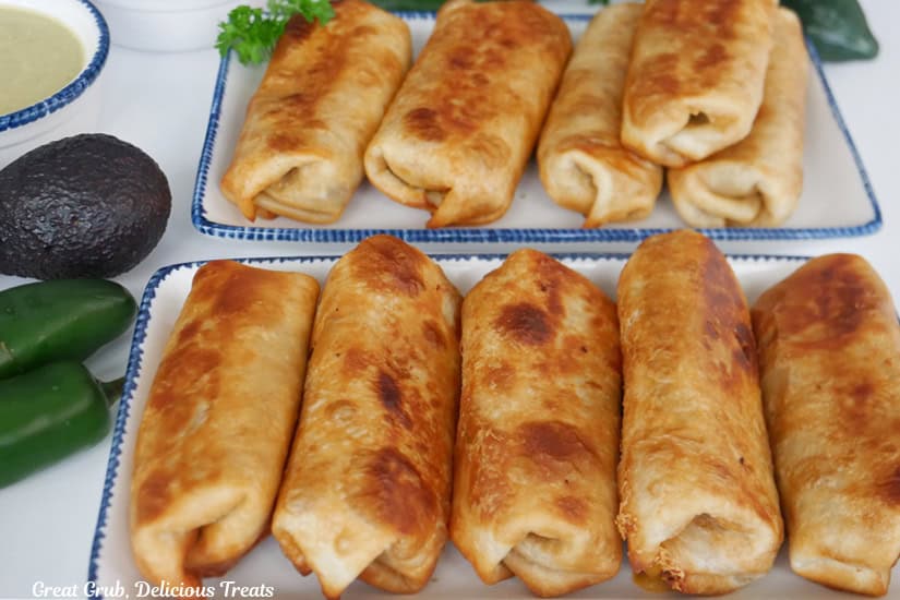 Two white rectangle plates with blue trim with five fried burritos on them.