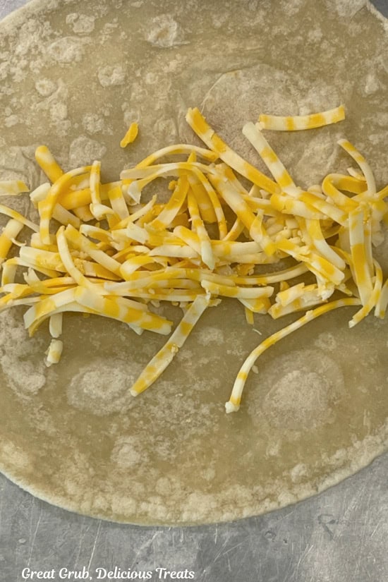 A flour tortilla with shredded cheese on it.