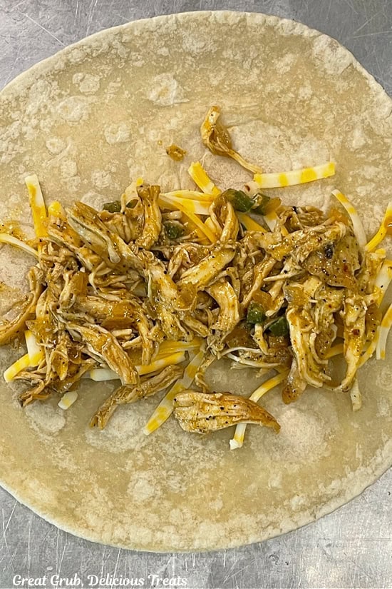 A flour tortilla with shredded cheese and shredded chicken.