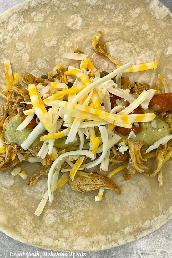 Shredded cheese, shredded chicken, poblano sauce, ranch beans, and more cheese all layered on top of a flour tortilla.