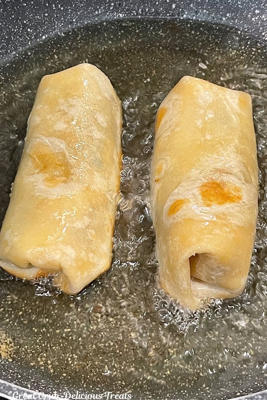 Two burritos in a hot pan of oil being fried.