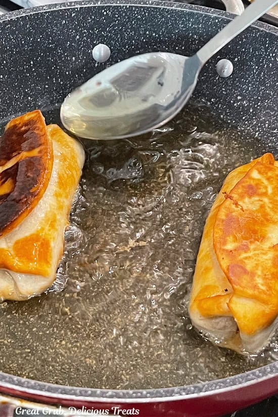 Two burritos in a pan with hot oil that are fried to golden perfection.