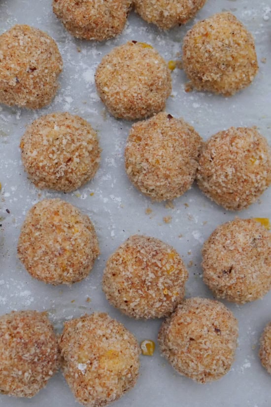 Breaded corn casserole bites on a baking sheet before being fried.