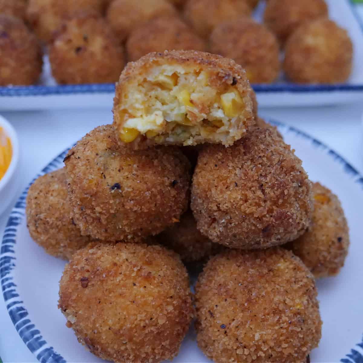 A white round plate with blue trim with a stack of fried corn casserole bites on it with a bite out of the top one.