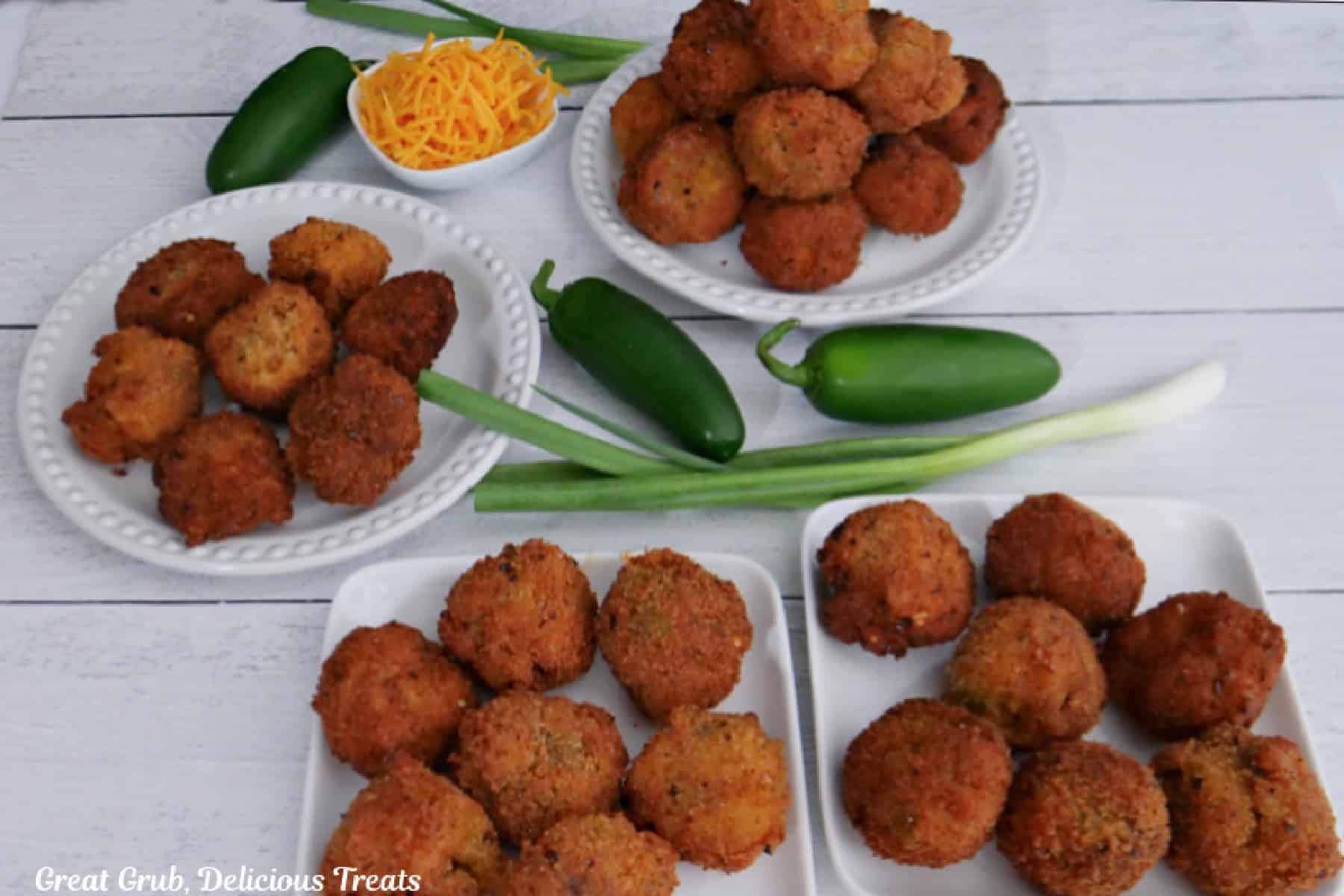 A white surface with four white small plates with a stack of fried mac and cheese bites on each plate.