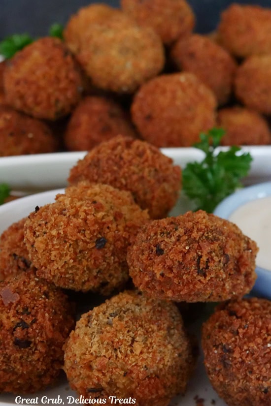A stack of meatloaf bites that are crispy and deep fried on a white plate with another white plate filled in the background.