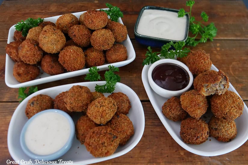 A wood surface with three white plates filled with bite-size meatloaf bites with dipping sauce.