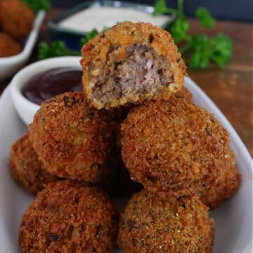 A white plate with a stack of deep fried meatloaf bites on it with a bite taken out of the one on top.