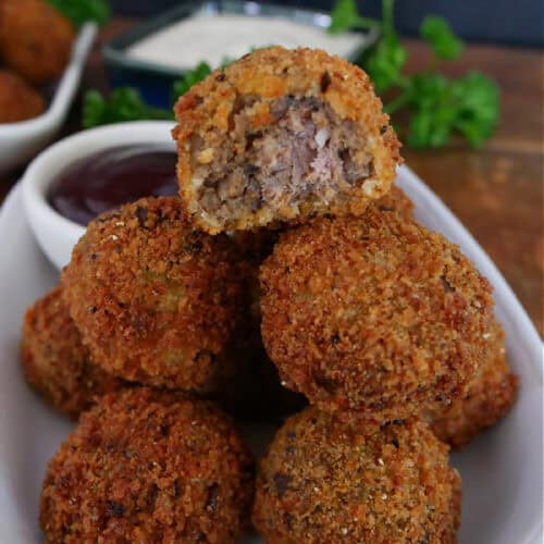 A white plate with a stack of deep fried meatloaf bites on it with a bite taken out of the one on top.