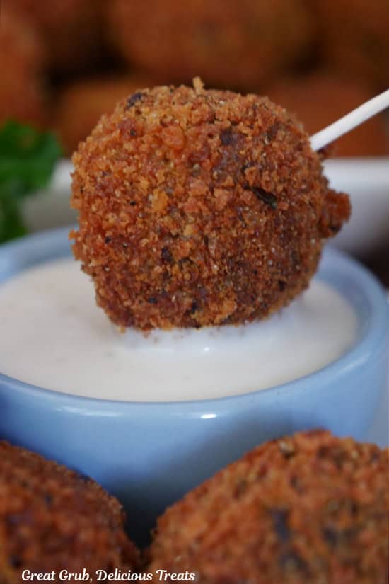 A deep fried meatloaf bite being dipped in dressing.