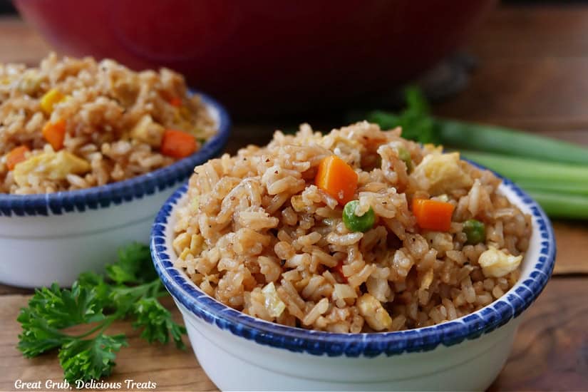 A wood surface with two white bowls with blue trim filled with fried rice on it.