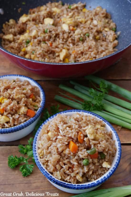 A wood surface with two white bowls with blue trim with a serving of fried rice in each one.