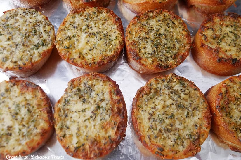 A baking sheet covered with aluminum foil and min round garlic breads on it.