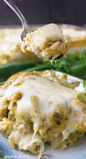 A bite of enchiladas held above the plate with a serving of enchiladas on it.