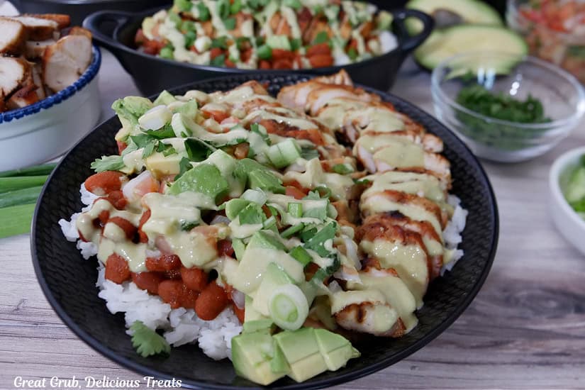 A black bowl filled with all the ingredients for grilled chicken burrito bowls with sauce drizzled over it.