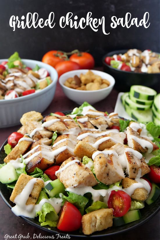 Two black bowls and a white bowl filled with salad, drizzled in ranch and a plate of sliced cucumbers in the background.