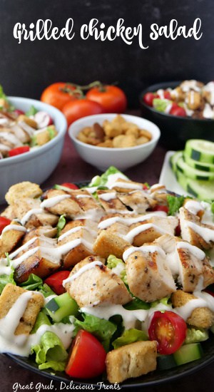 Grilled Chicken Salad is a refreshing and crispy salad that is loaded with tender, juicy chicken breast, cherry tomatoes, cucumbers, and drizzled with ranch dressing and topped with croutons. A black bowl filled with salad and drizzled with ranch dressing.