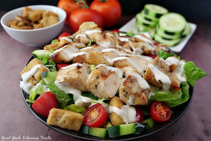 Grilled Chicken Salad is a healthy and light salad recipe that is perfect for lunch. A close up picture of salad in a black bowl, topped with chicken, ranch dressing, and croutons.