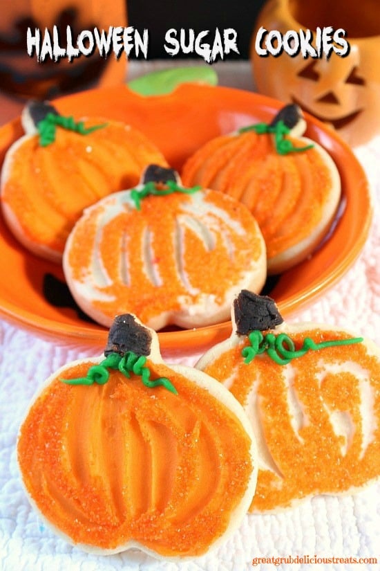 A white surface with pumpkin shaped cookies with orange frosting on them.