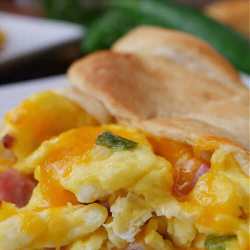 A breakfast crescent filled with eggs, ham, and cheese on a white plate.