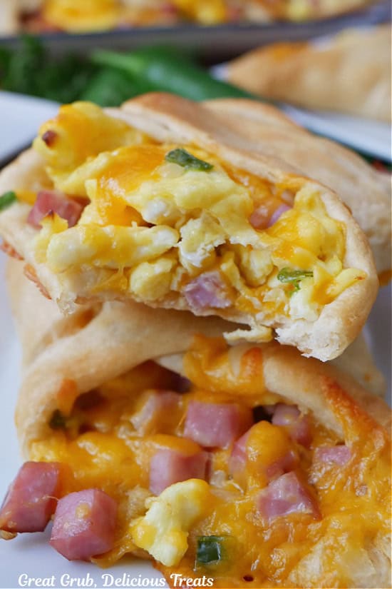 A white plate with two breakfast crescent rolls filled with eggs, ham, and cheese.