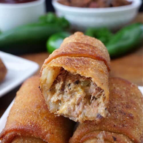 Three fried egg rolls on a white plate with a bite taken out of one of them.
