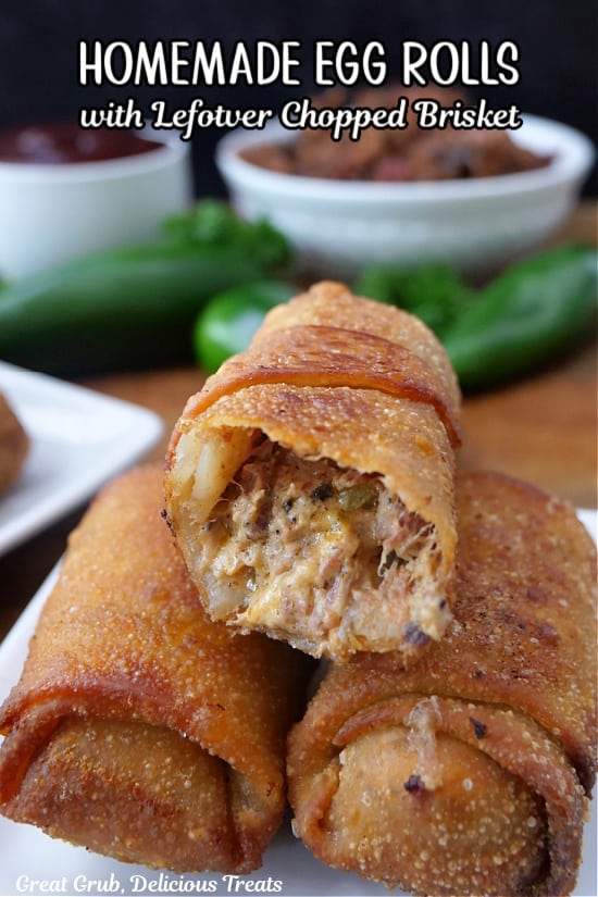 Three fried egg rolls on a white plate with a bite taken out of one of them.