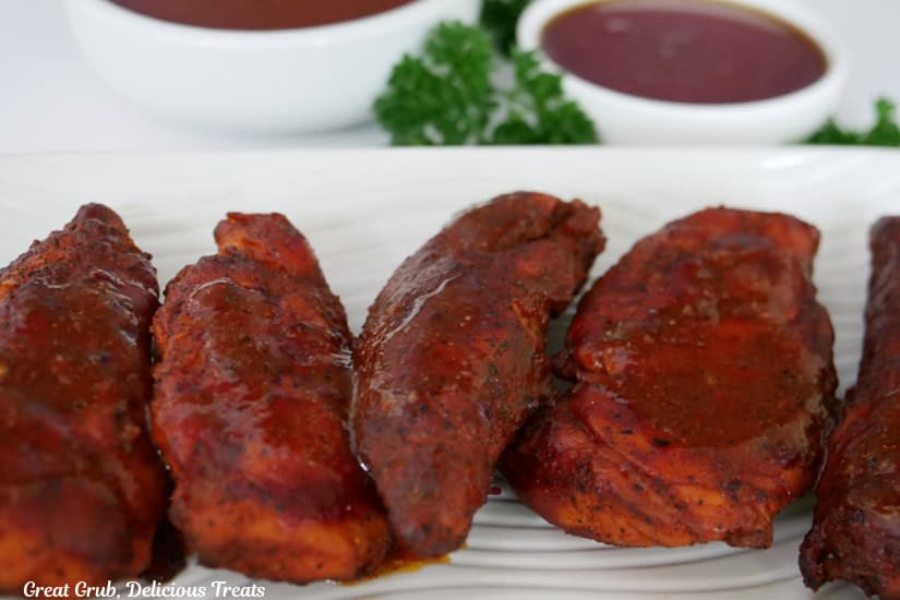 A white oblong plate with five smoked hot honey chicken strips on it.