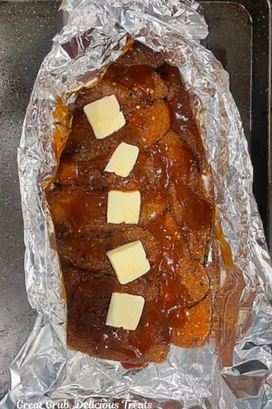 Chicken strips topped with hot honey, BBQ sauce, and pads of butter before being wrapped up in aluminum foil.