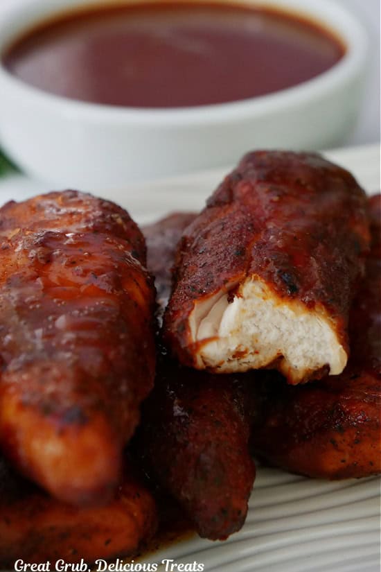 A few smoked chicken strips on a white plate with a bite taken out of one of them.