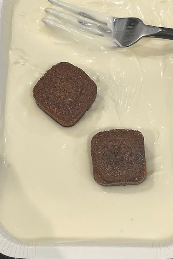A carboard tray with melted white chocolate in it with two mini gingerbread bites about to be covered in chocolate.