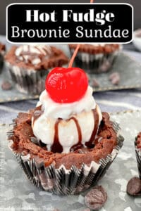 A close up photo of one brownie cup, in a black and white plaid cupcake liner, topped with ice cream, hot fudge, and a cherry.