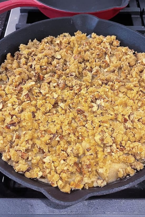A cast iron pan placed on the smoker grill filled with peach cobbler before it has been smoked.