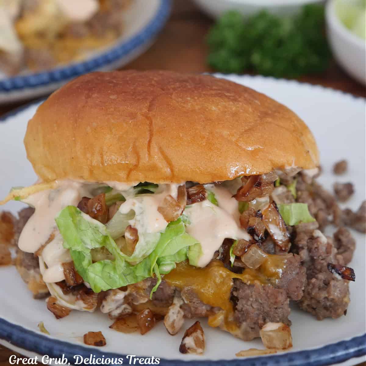 A round white plate with blue tri with a beef slider on it showing the ground beef, lettuce, grilled onions, and the copycat In N Out spread.
